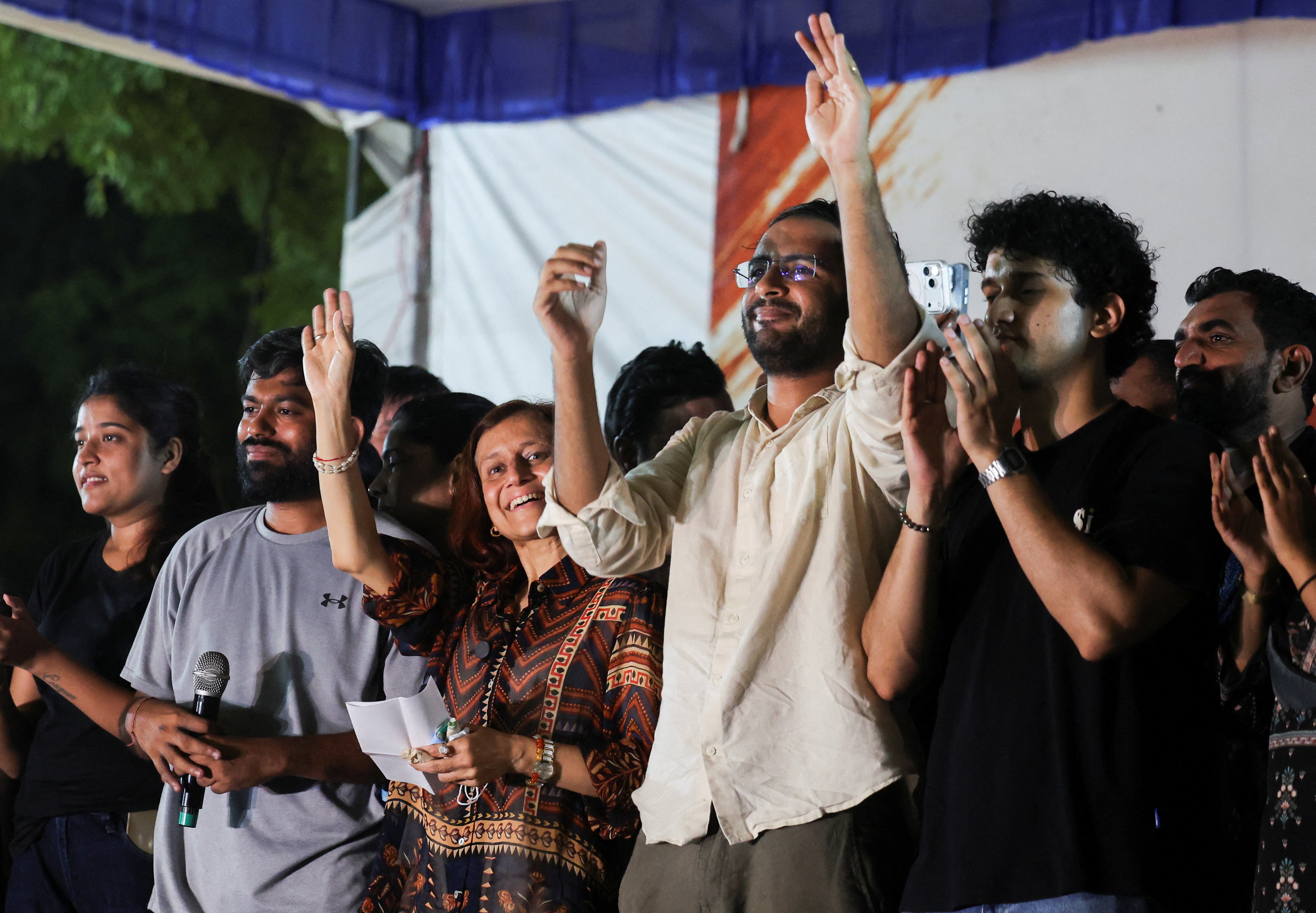 A group of men and women on a stage waving. 