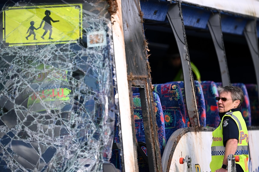 A shattered windscreen of a bus with no windows and a police officer looking in