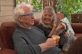 A man and woman sit on a sofa holding mugs.