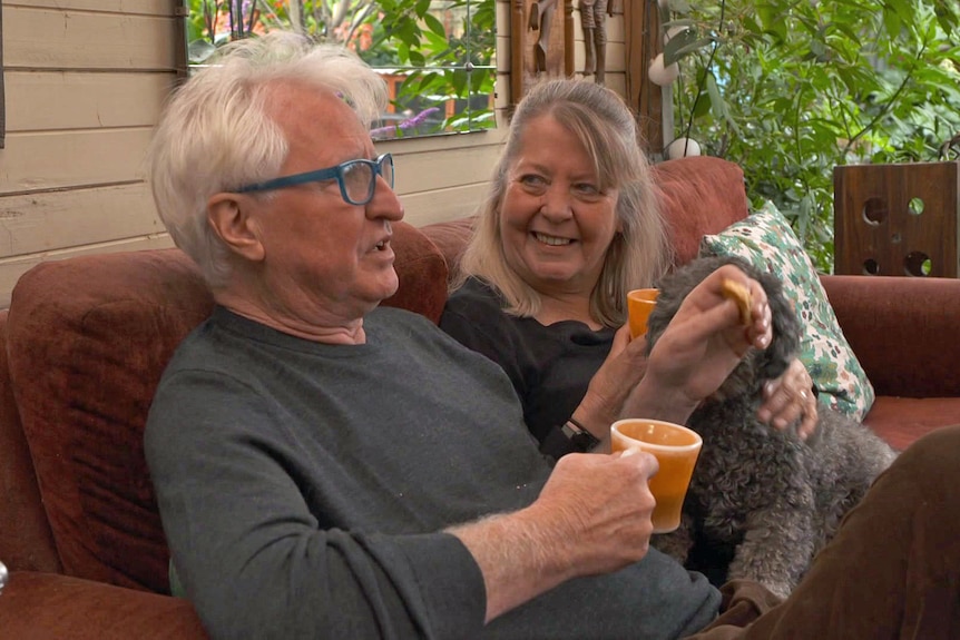 A man and woman sit on a sofa holding mugs.