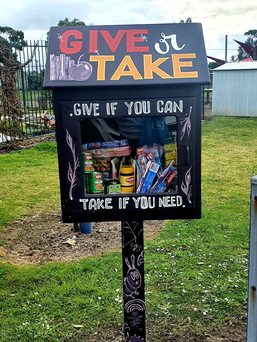 A painted wooden box full of pantry items like vegemite and canned food