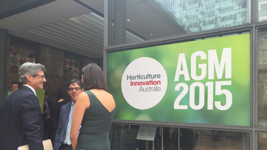 People talk near a poster of the AGM 2015 for Horticulture Innovation Australia