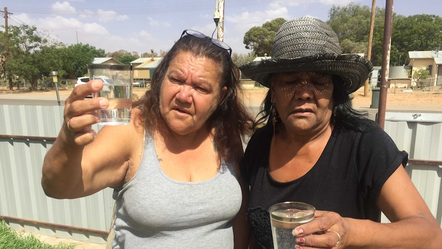 Two women hold up glasses of water in a far-west NSW town.