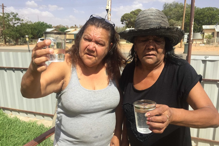 Two women hold up glasses of water in a far-west NSW town.