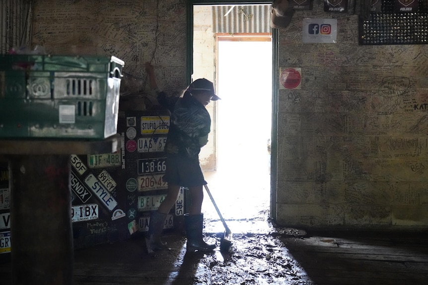 A young girl sweeps mud, water and debris from a building's floor.