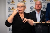 A female Auslan interpreter signs emergency information to a camera in front of an ACT Government banner.