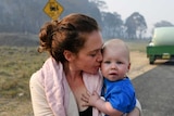 A woman waits at a road block on the road while holding a baby