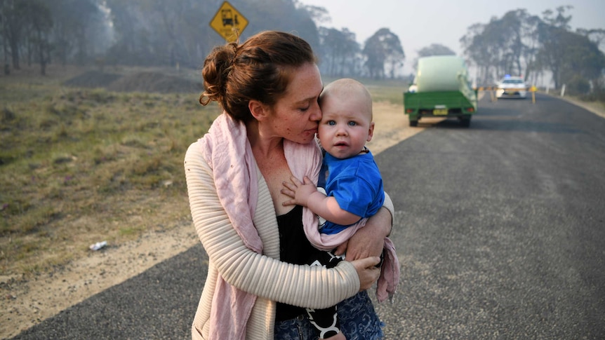 A woman waits at a road block on the road while holding a baby