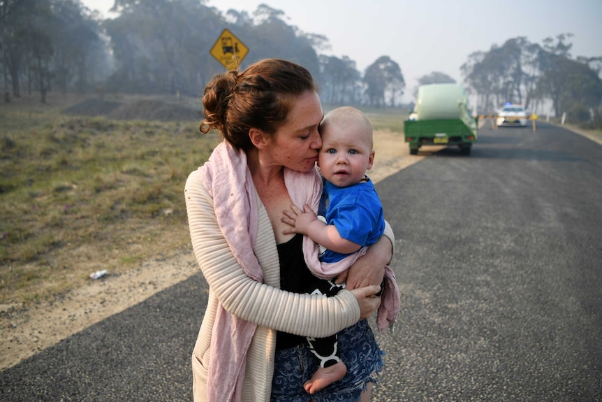 A woman waits at a road block on the road while holding a baby