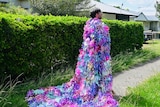 An image of the back of a man wearing a multi-coloured tinsel jacket infront of a hedge 