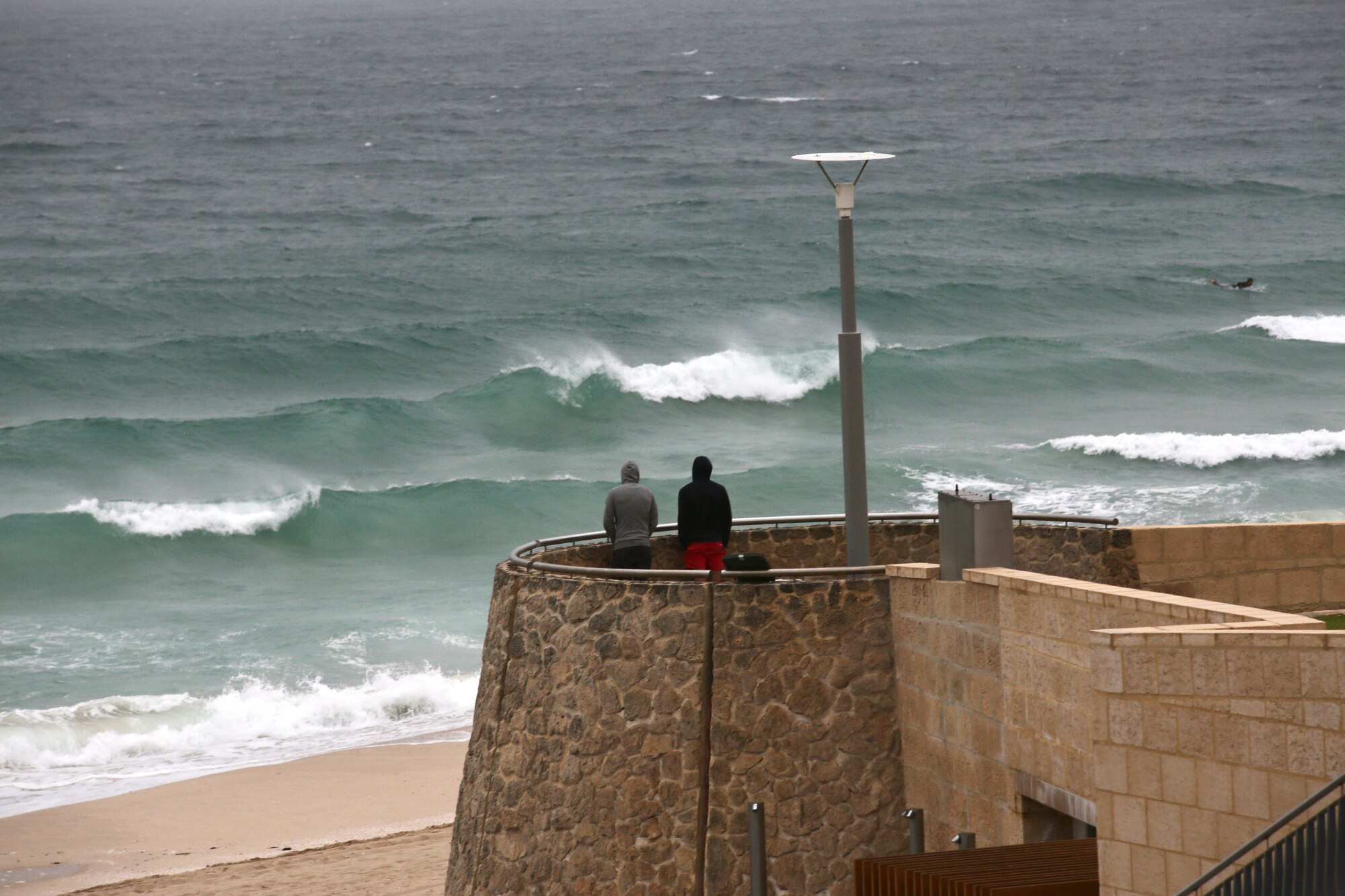 2  men stand on a lookout at Scarborough watching huge lines of swell roll in as a storm approaches.