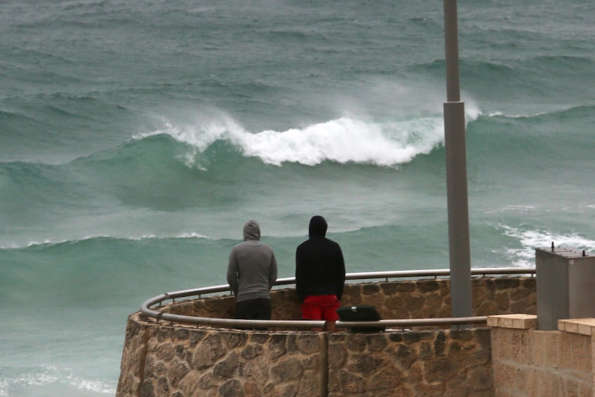 2  men stand on a lookout at Scarborough watching huge lines of swell roll in as a storm approaches.