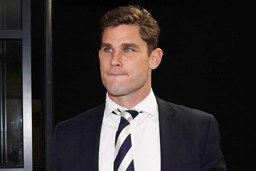 A male AFL player wearing a suit and tie walks into a building.