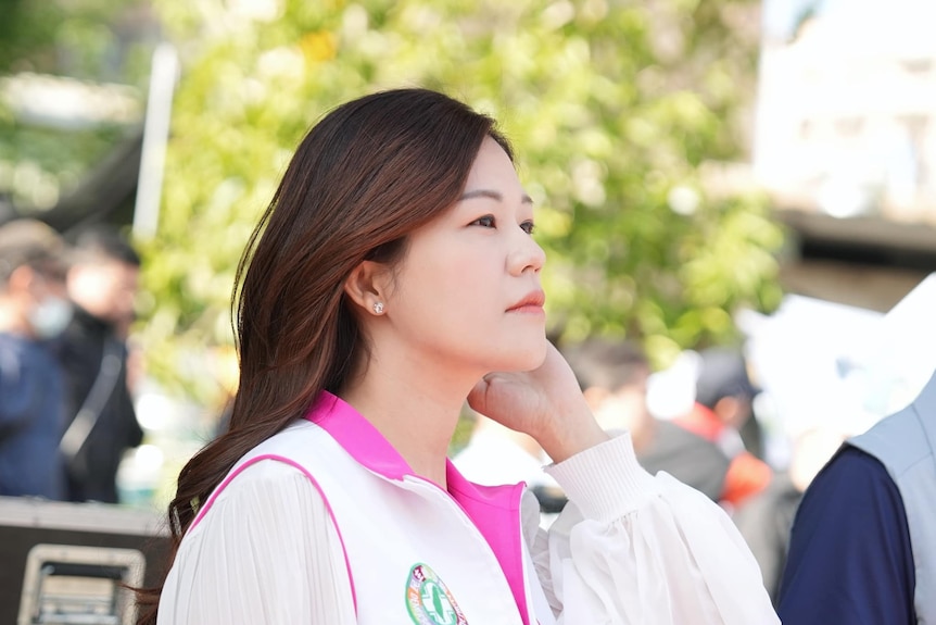 A young woman wearing a white top with hot pink collar looks up on a bright day
