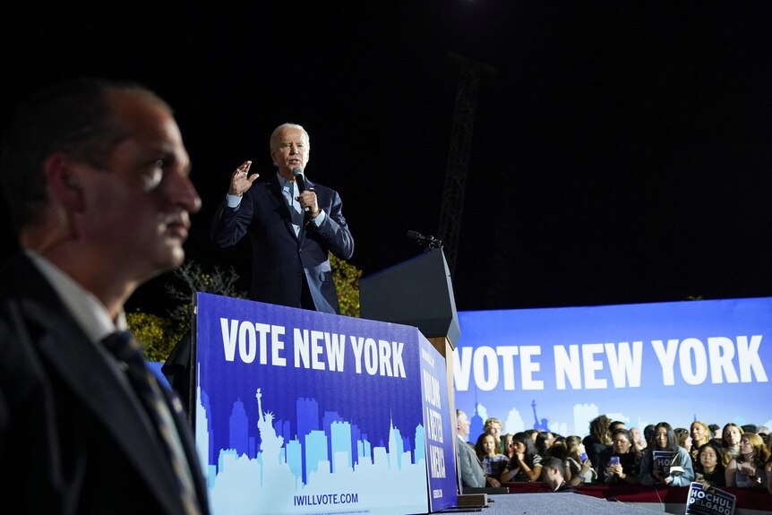 Joe Biden speaks onto a microphine as crowds watch on