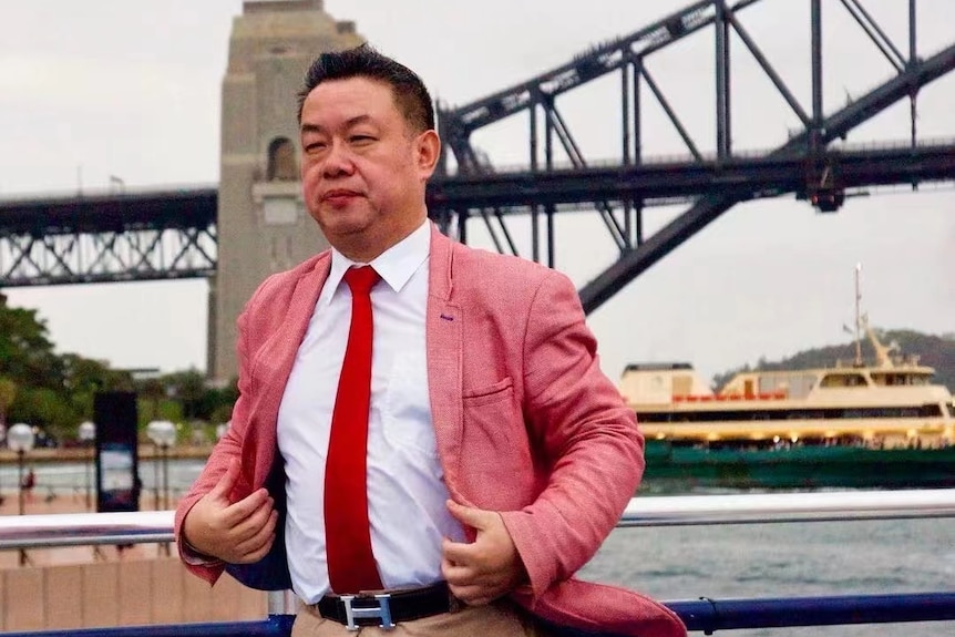 A man in a pink suit stands in front of the Sydney Harbour Bridge.