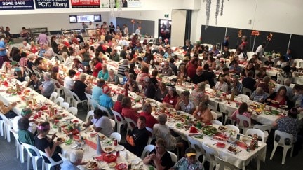 A crowd of people sitting at tables having Christmas Day lunch