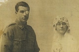A man wearing his army uniform is standing next to his bride in a white wedding gown with a large bunch of flowers