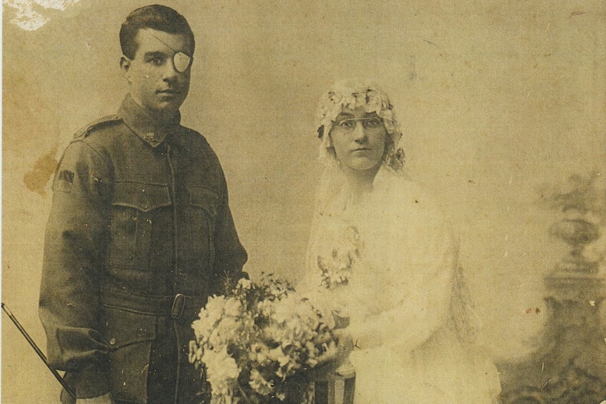 A man wearing his army uniform is standing next to his bride in a white wedding gown with a large bunch of flowers