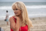 Lily James on a beach wearing a red swimsuit, portraying Pamela Anderson
