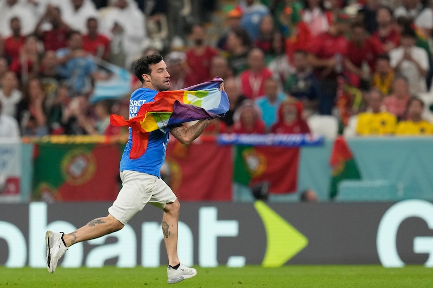 A man runs across a field carrying a rainbow flag