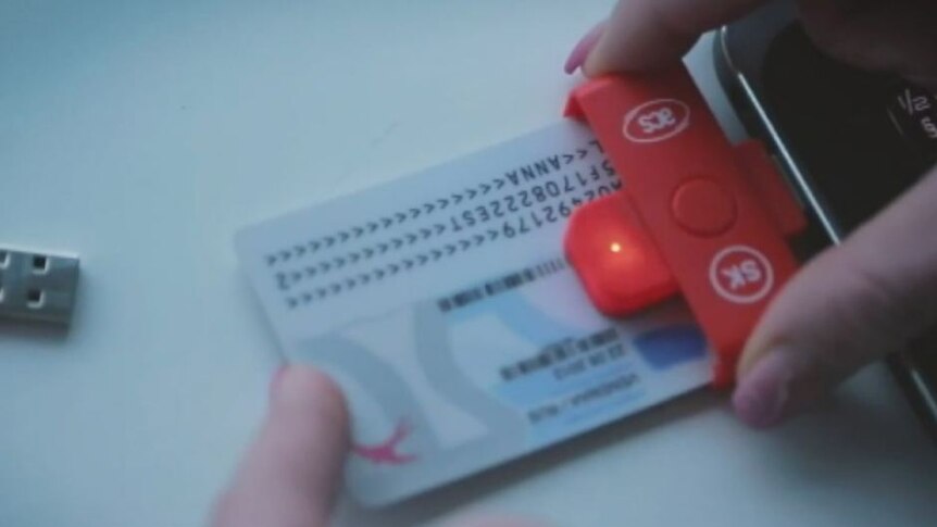 A white credit card sized card with numbers and letters is inserted into a reader attached to a smart phone