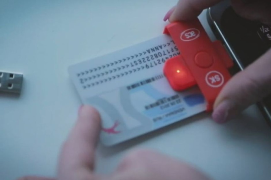 A white credit card sized card with numbers and letters is inserted into a reader attached to a smart phone