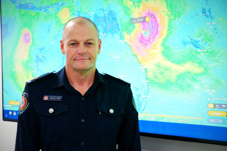 A man stands in front of a large screen displaying a map of a cyclone off the Queensland coast.