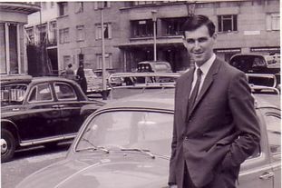 Black-and-whtie photo of a man standing in front of a VW Beetle in 1960.
