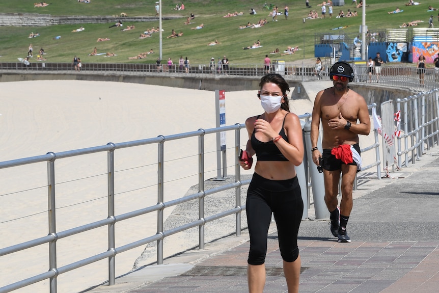 A woman in a face mask jogs along the boardwalk at Bondi Beach.