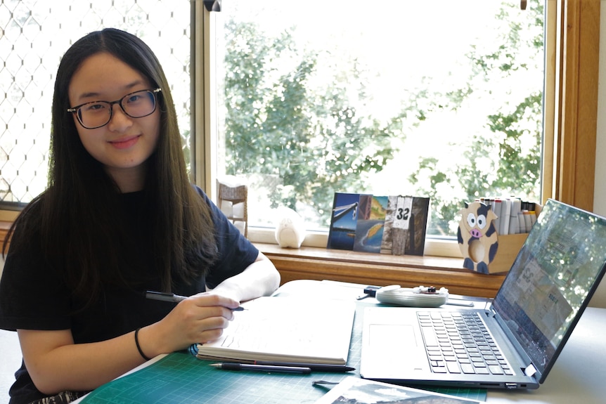 A young woman sits at her desk beside a window.