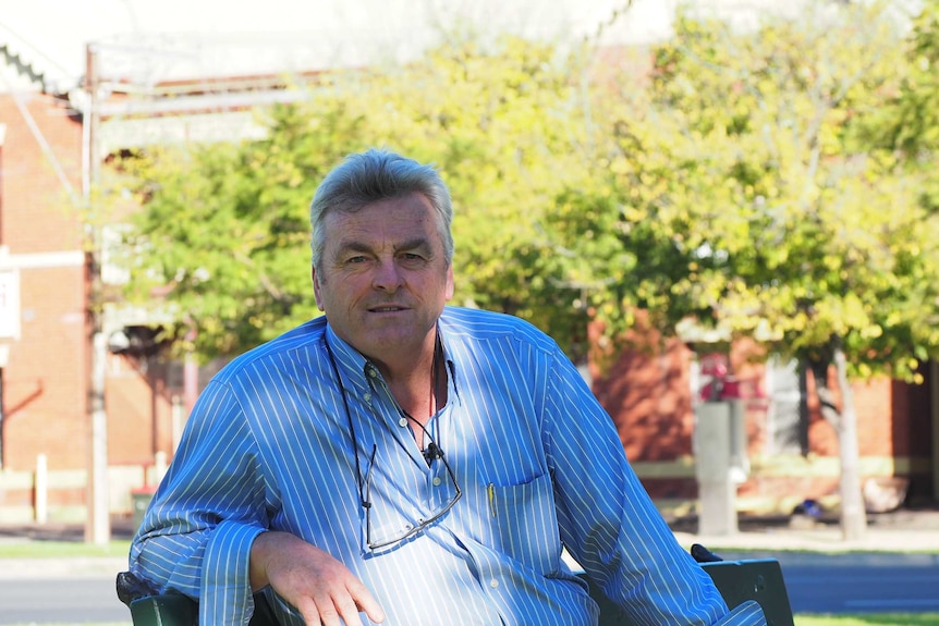 A man in a blue business shirt sits on a bench.