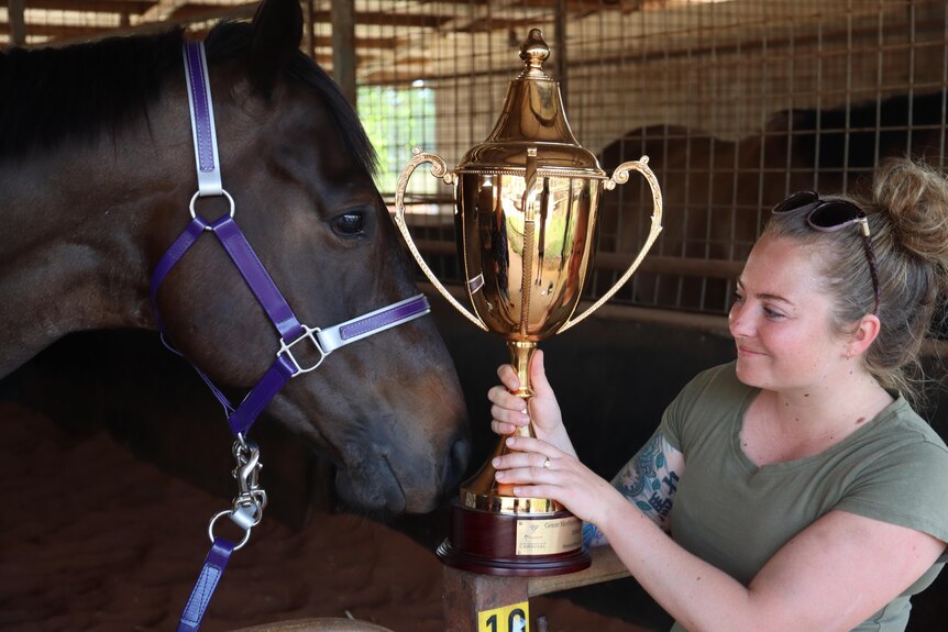 Jockey Jessie Philpot holds the Darwin Cup trophy next to the winning horse Highly Decorated.