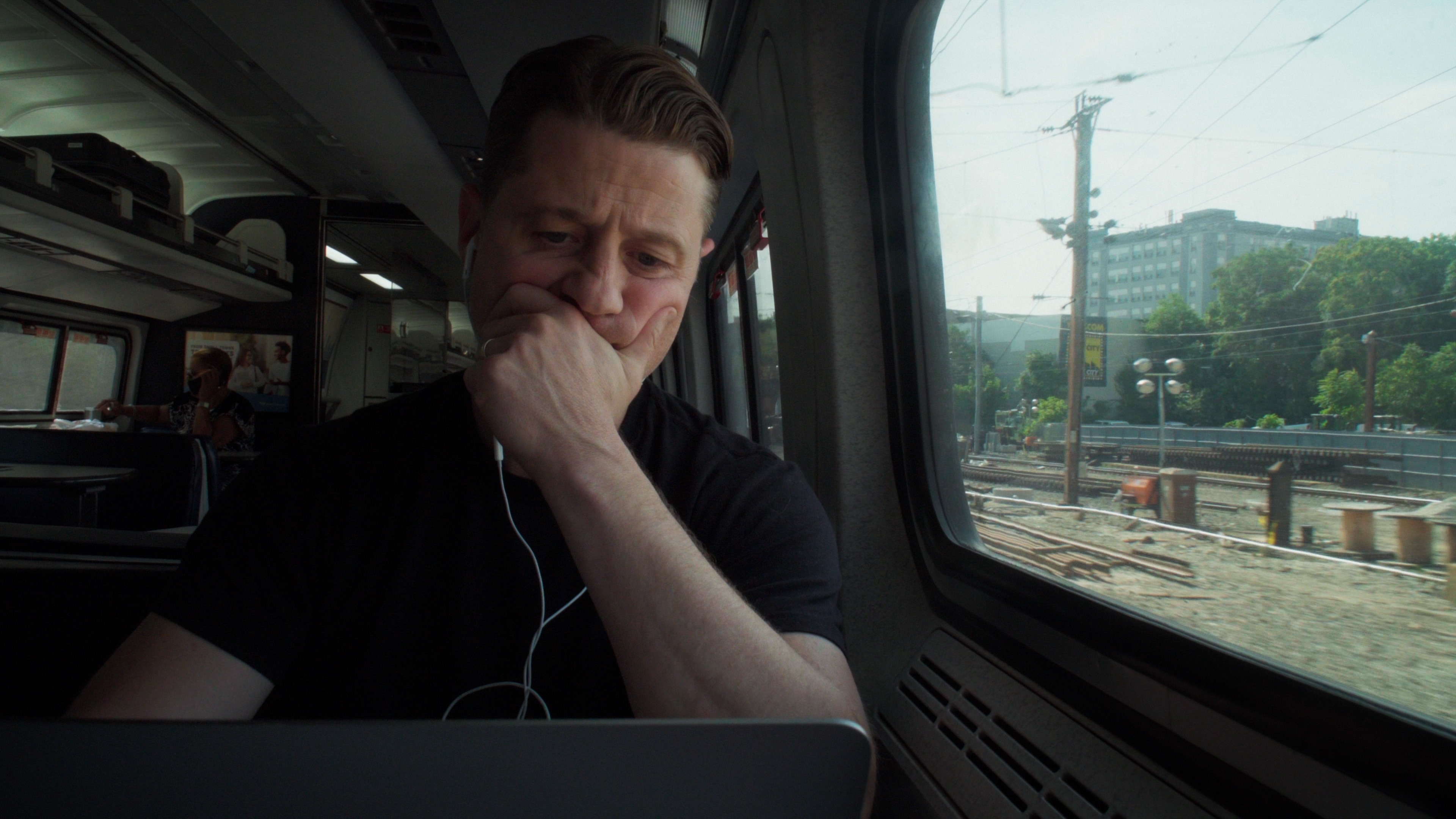 Ben McKenzie looking at a laptop critically while on a train.