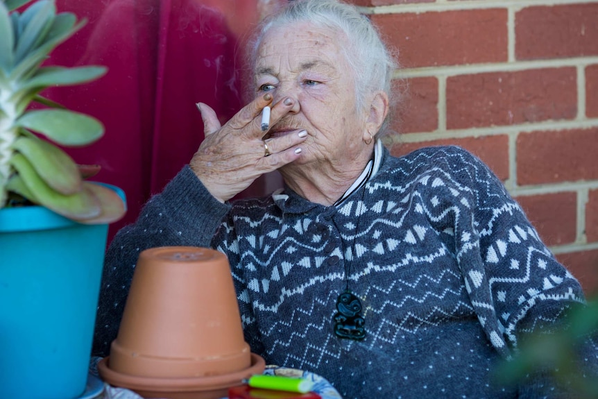 Bev Howlett with her hand over her mouth as she smokes a cigarette.