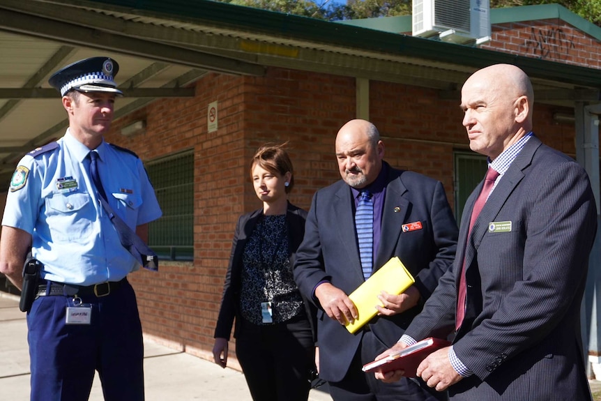 A uniformed police officer stands with three detectives in front of a brick building at Hudson Park