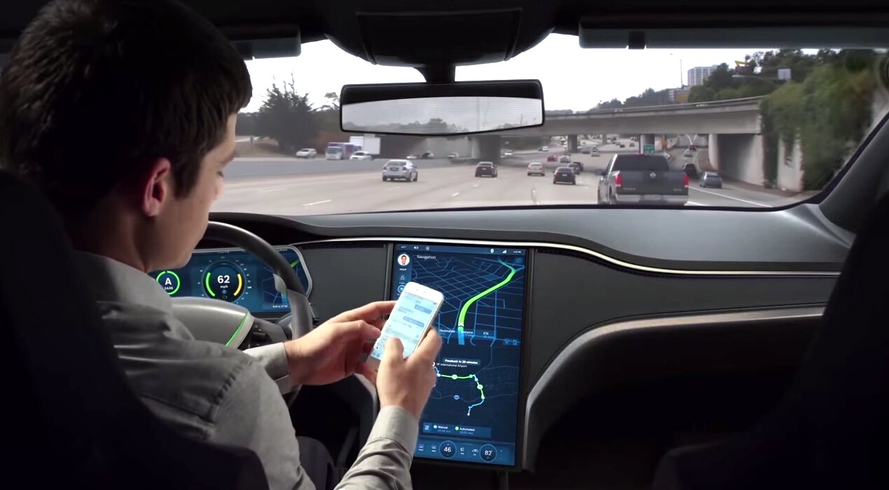 A driver uses his mobile phone while in a driverless car on a multi-lane freeway.