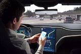 A driver uses his mobile phone while in a driverless car on a multi-lane freeway.