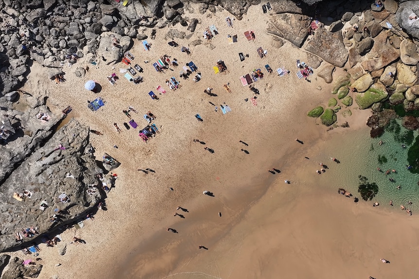 A birds eye view of a small bay with people sunbaking on the beach. 