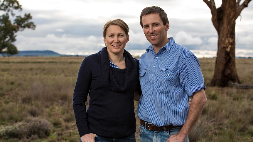 Medium profile shot of two people standing with a grassy paddock in the background.