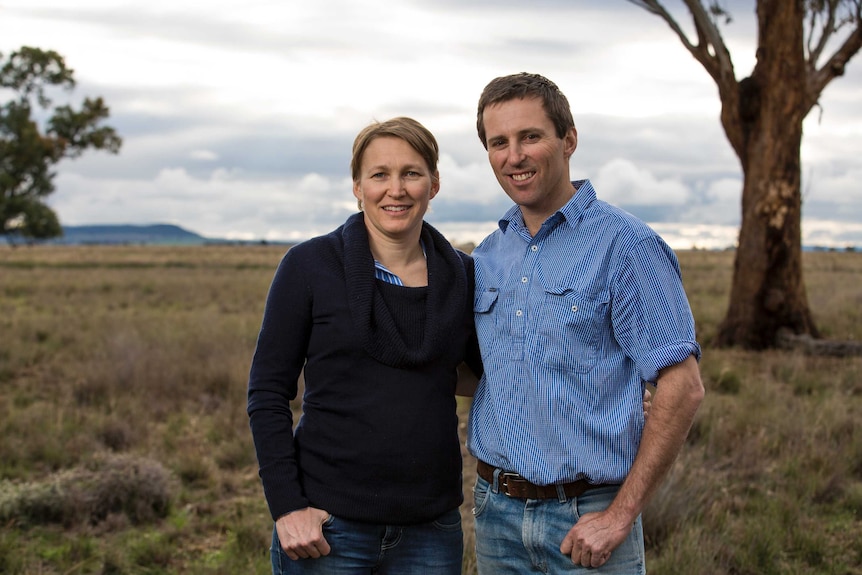 Medium profile shot of two people standing with a grassy paddock in the background.