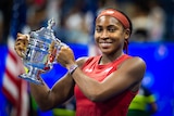 A woman wearing a red top and a red headband, holds aloft a trophy