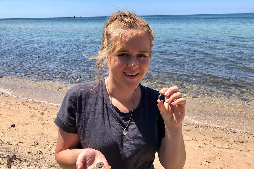 A young woman standing at beach holding a handful of metal finds