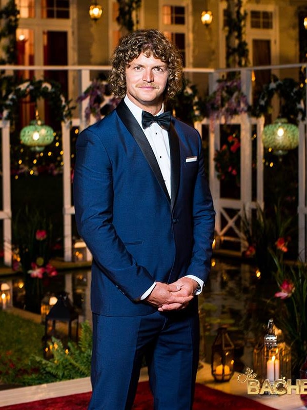 Nick Cummins stands in a suit on set of The Bachelor.