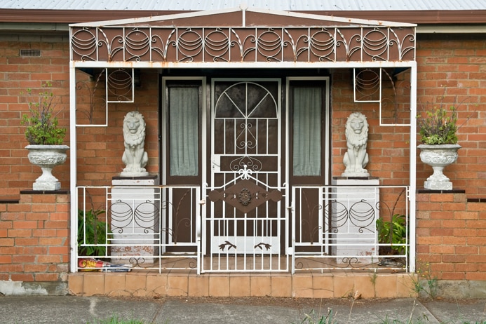 You view an ornate entrance to a house with two stone lions on plinths beside a brown front door.