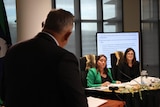 Two women in a meeting room being questioned by a man