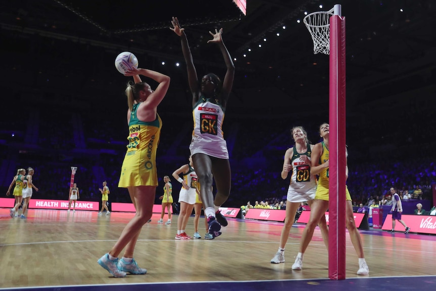 A netballer gets ready to shoot for goal as her opposing defender leaps to block her.