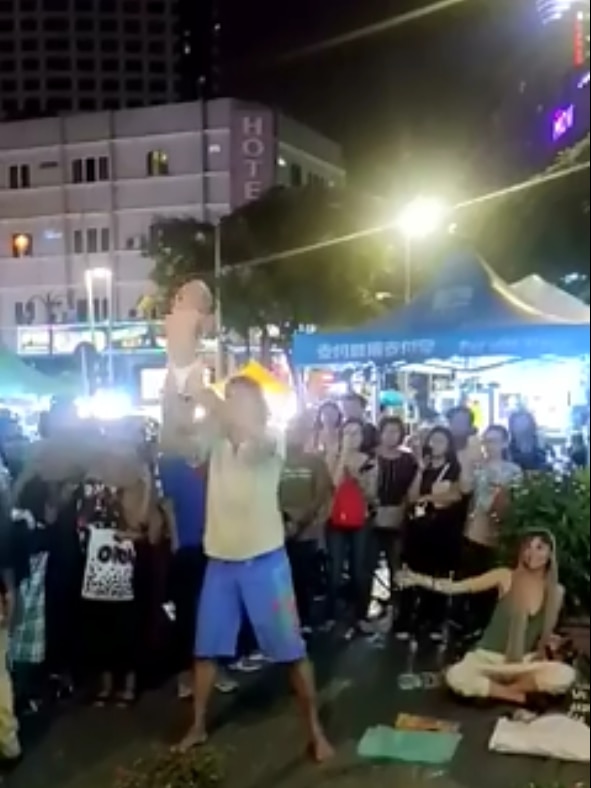 A Russian man holds a baby up in Malaysia street performance.
