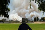 A person watches a large bushfire burning in the distance.