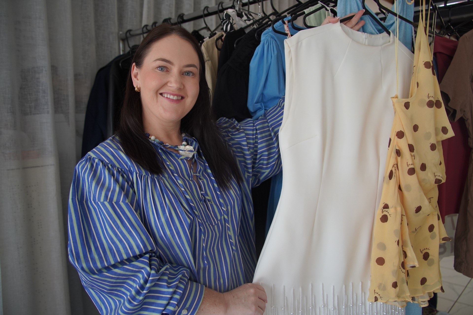 Una mujer con una camisa a rayas azules y blancas sostiene un vestido junto a un perchero